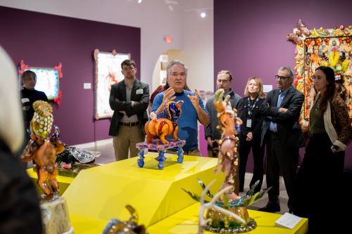 museum employee speaking to a group of visitors as he stands next to a small sculpture